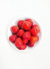 Close-up of strawberries in a small white plate on a white background. Top of view. 