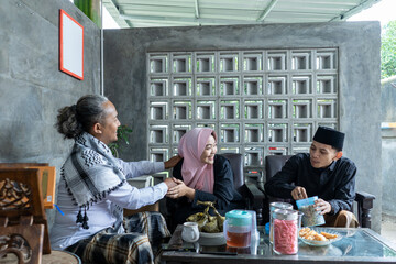 Senior men with long hair sit on the sofa with their younger guests and kiss their hands. Asian Muslim traditions on Eid al Fitr