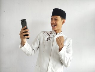 Moslem Asian man clenched fist showing excitement when looking to his mobile phone