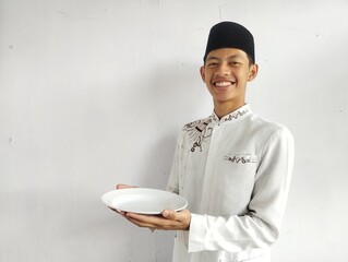 Moslem Asian man smiling at the camera while holding empty dinning plate