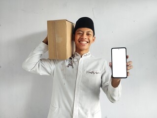Moslem Asian man smiling happy while bring a luggage and showing blank handphone screen
