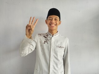 Moslem Asian man smiling at the camera and showing three fingers sign