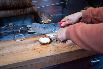 Close-up of hands slicing kokorec, a traditional Turkish street food made from seasoned lamb intestines, on a wooden board.