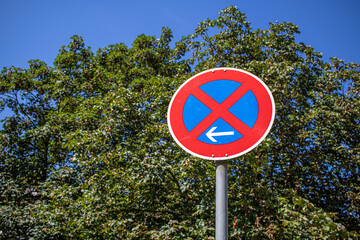 German clearway traffic sign indicating an absolute ban on stopping to the left of the sign, with trees and blue sky in the background