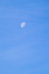 A clear image of a crescent moon visible during the daytime against a vibrant blue sky, highlighting a serene natural phenomenon.