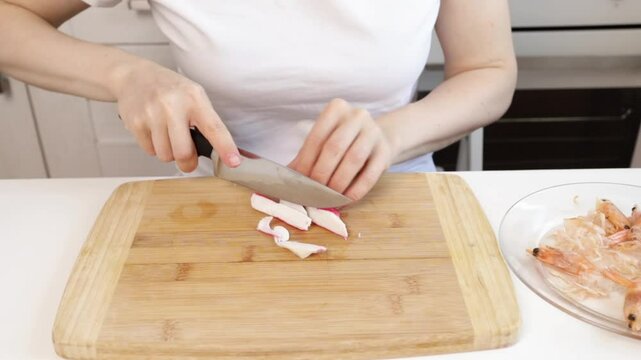 Hands cutting crab meat, knife chopping surimi sticks, culinary routine during lunch.