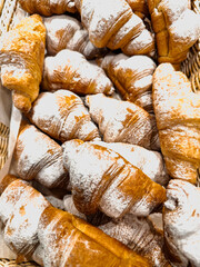 Freshly baked croissants dusted with powdered sugar displayed in a woven basket at a bakery