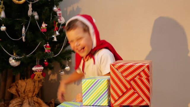 Christmas morning, young boy wearing Santa costume play with metal spring. He launch it to tumble down from heap of colorful Christmas present boxes, close portrait shot