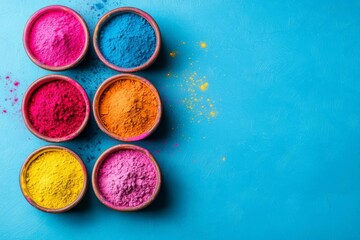 Bright colored powders in bowls against a blue background for vibrant festivals.