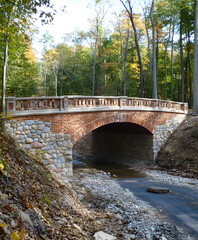 Fototapeta premium A charming stone bridge arches over a small stream, surrounded by lush trees, blending nature with rustic architecture