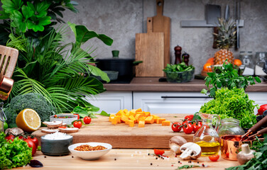 Healthy eating, cooking, food blogging background. Pumpkin cut into cubes on oak cutting board with vegetables, herbs and spices on cozy kitchen with wooden table, kitchenware 