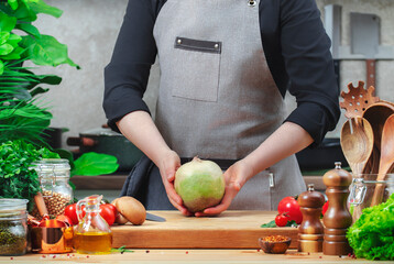 Chef holding large margellan radish in hands. Cozy kitchen with wooden table, kitchenware, vegetables, herbs and ingredients for cooking. Healthy vegan eating, culinary, recipes, food blogging comcept