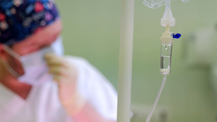 Surgeon preparing for surgery in hospital operating room, wearing face mask and with iv bag in foreground