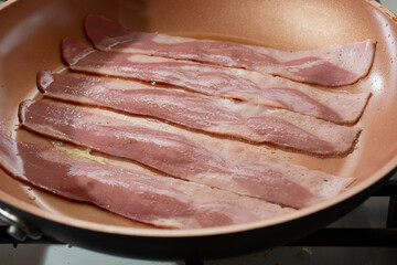A view of strips of turkey bacon frying in a ceramic skillet.