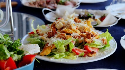 Close up caesar salad with grilled chicken, crispy croutons, ripe tomatoes, grated parmesan cheese nestled on white ceramic plate over blue linen background