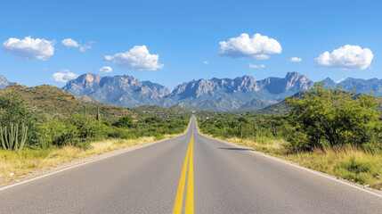 Naklejka premium scenic road stretches through desert landscape with mountains in background, showcasing clear blue sky and fluffy clouds