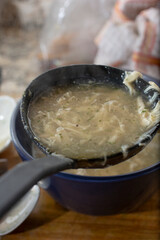 A view of a ladle scooping some chicken gravy from a bowl.
