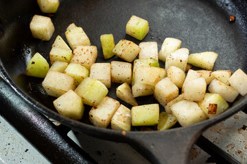 A view of chopped kohlrabi cooking in a cast iron skillet.