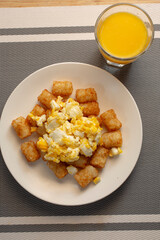 A top down view of a plate of tater tots and scrambled eggs.