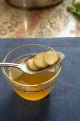 A view of ginger slices on a spoon, above a glass bowl of bone broth.