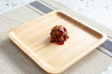 A view of a single grape jelly meatball on a wooden plate.