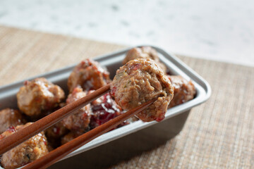 A closeup view of a pair of chopsticks holding a grape jelly meatball.