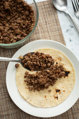 A top down view of a spoonful of ground bison meat over a corn tortilla.
