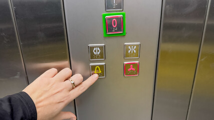 A Caucasian hand pressing the elevator alarm button, symbolizing urgency and safety concerns in public transportation settings