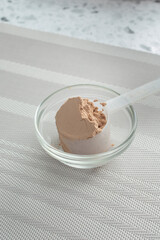 A view of a measuring scoop pouring protein powder into a small glass bowl.