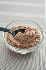 A view of a spoon scooping some protein powder from a small glass bowl.