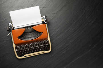 Vintage typewriter with sheet of paper on black background, top view. Space for text