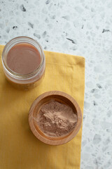 A top down view of a protein shake in a glass mason jar, and protein powder in a wooden bowl.
