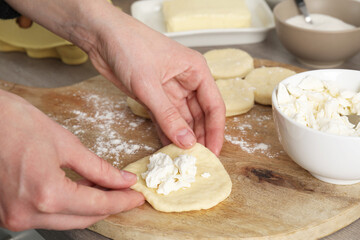 Woman making pirozhki (stuffed pastry pies) with cottage cheese at table, closeup