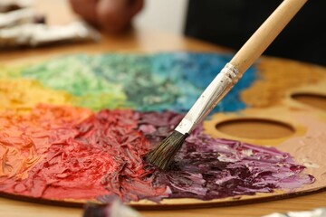 Mixing paints on palette with brush at table, closeup