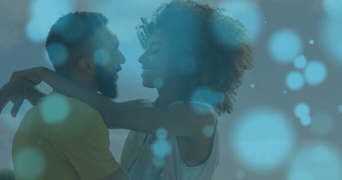 Image of light spots over biracial couple embracing at seaside