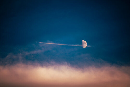 Airplane Leaving a Contrail Across the Half Moon in the Twilight Sky