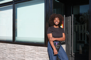 Young smiling hairdresser standing at the entrance of her shop
