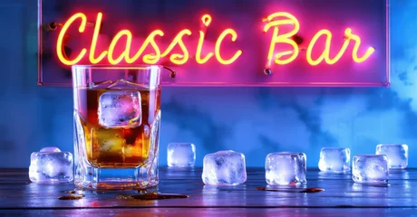 Neon sign reading Classic Bar glows in warm orange tones above a bar counter, featuring a chilled cocktail with an orange slice, surrounded by scattered ice cubes under soft lighting