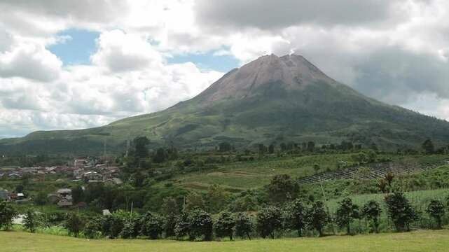 Mount Sinabung under cloudy skies, creating a dramatic and moody volcanic landscape. Perfect for nature and documentary projects.