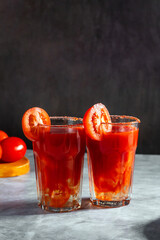 Two vegetable shaken cocktails in glass on dark grey background. Red tomato cocktail. Served with tomato slice. Vegan menu.