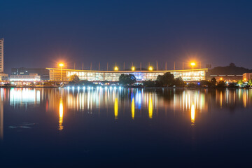 Obraz premium Vibrant Night View of an Illuminated Stadium by the Water