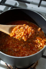 A view of a wooden spoon scooping some jambalaya soup out of a stockpot.