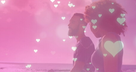 Image of hearts falling over biracial couple walking at seaside