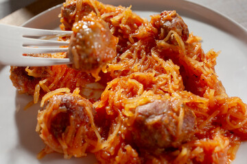 A view of a fork picking up a meatball from a plate of spaghetti squash and meatballs.