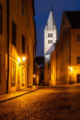 View from Jirska Street showcases the Bell Tower of St. George's Basilica illuminated by streetlights. The cobblestone path adds a historic charm to the Prague Castle area during nighttime.