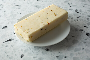 A view of a block of pepper jack cheese, on a plate.
