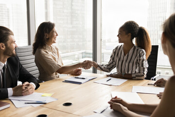 Two multinational businesswomen shaking hands, gesture of successful meeting or negotiation...