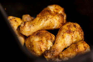 Close up an open air fryer with roasted chicken drumsticks inside
