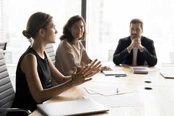 Professional businesswoman speaks to shareholders met in boardroom, reviewing Document data,...