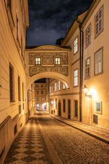 This quiet street showcases the passage bridge of the Chamber of Deputies, illuminated by soft light, framed by historic buildings along Thunovska Street in Lesser Town, Prague.